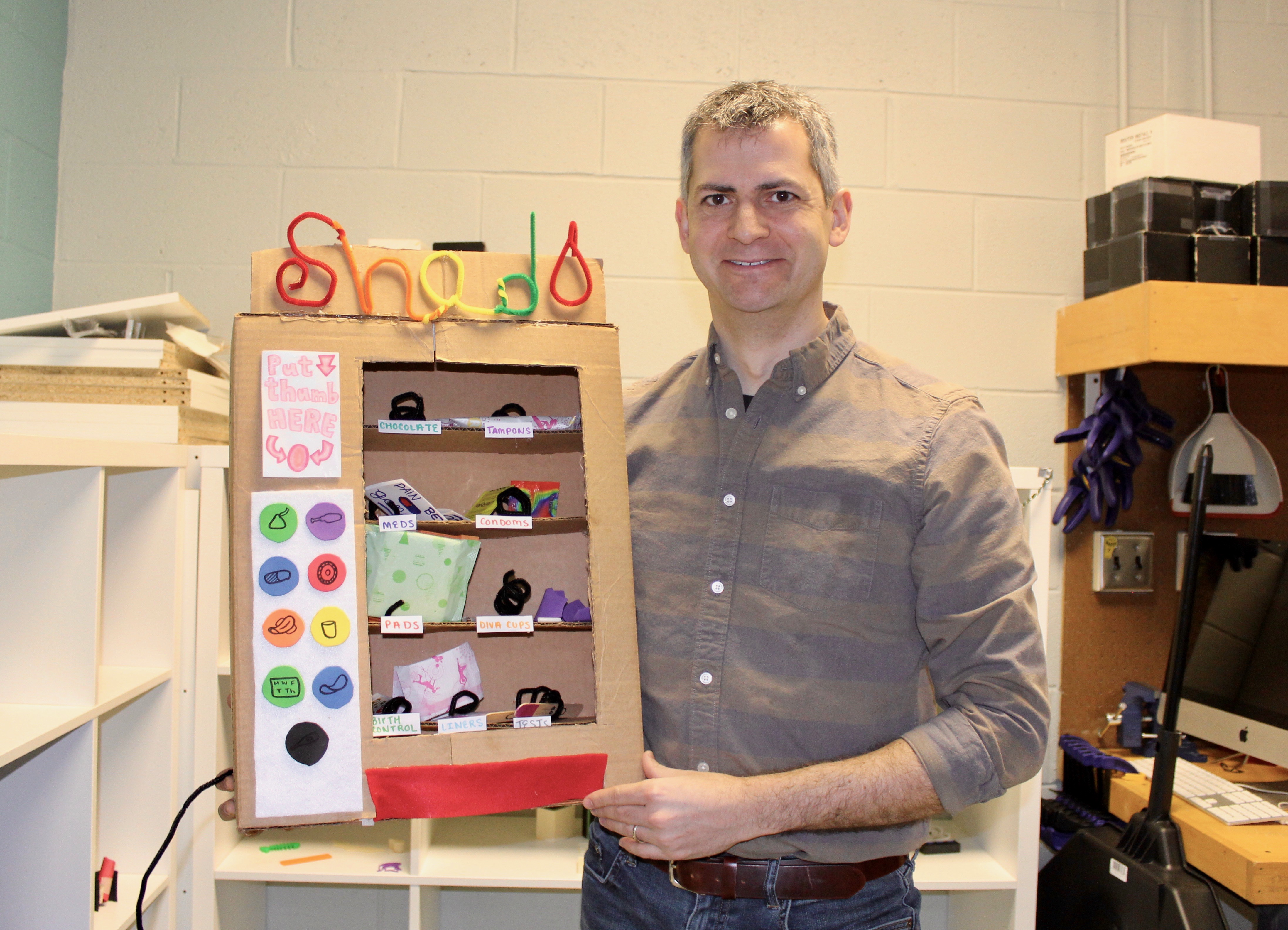 Isaac posing with a student project, the shed vending machine for women's reproductive health. Photo credit: Piper Cook, LBC